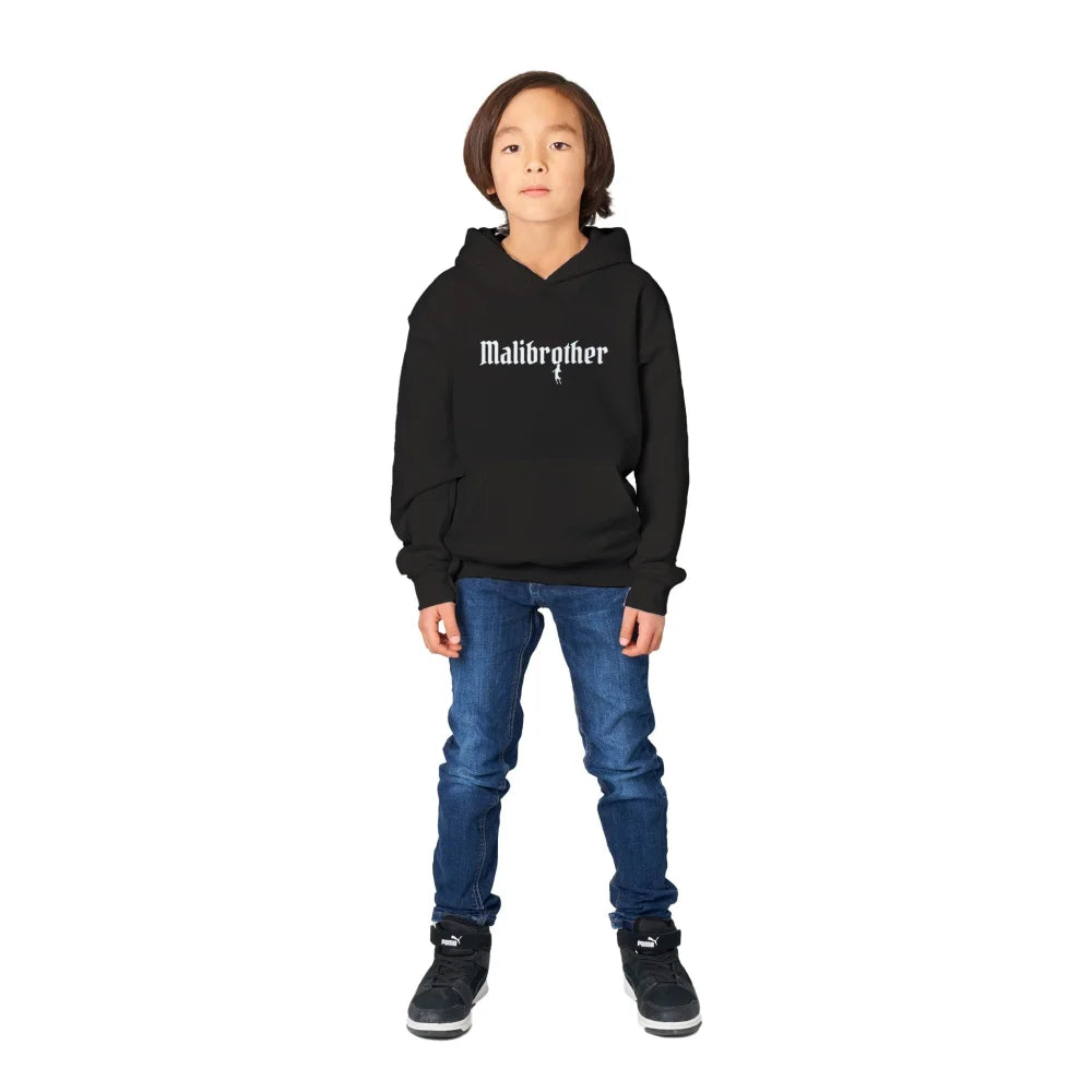 Enfant portant un sweat à capuche noir avec le texte ’Maidenform’, un jean bleu et des baskets foncées.