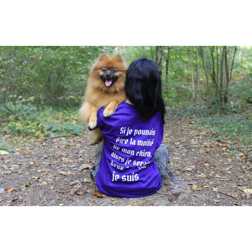 Une personne portant une chemise violette avec un texte en français et tenant un chien de Poméranie en peluche.